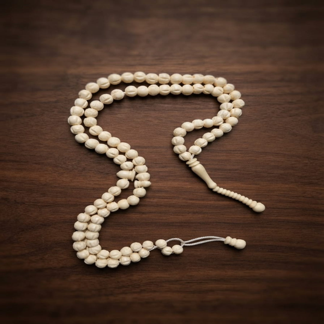 A strand of cream-colored wooden prayer beads (tasbih) with a matching wooden tassel, arranged on a dark brown wooden surface.