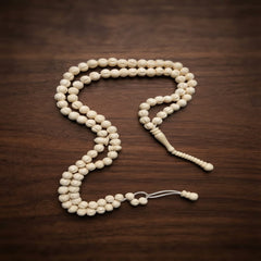 A strand of cream-colored wooden prayer beads (tasbih) with a matching wooden tassel, arranged on a dark brown wooden surface.